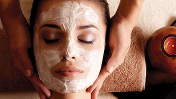 A person receiving a facial treatment with a towel and a candle on a table.