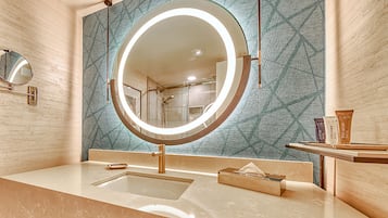 A bathroom with a round mirror, a sink, and a vanity with toiletries.