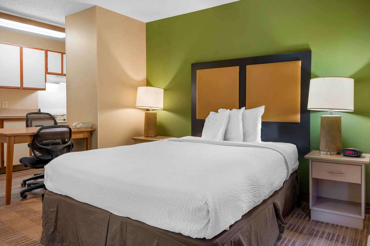 Una camera d'albergo con un letto, una scrivania, una sedia, un comodino e una lampada.