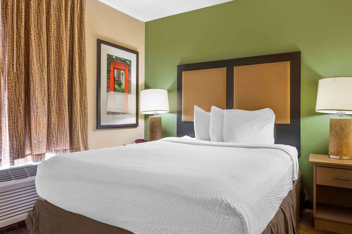 Una camera d'albergo con un letto grande, due abat-jour, un quadro incorniciato appeso al muro e una finestra con tende.