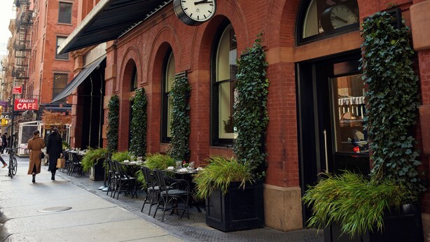 A brick building with outdoor seating, a clock, and a cafe sign. - The Mercer (New York)