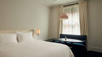 Una habitación de hotel con una cama grande, una mesita pequeña, un banco y una ventana con cortinas.