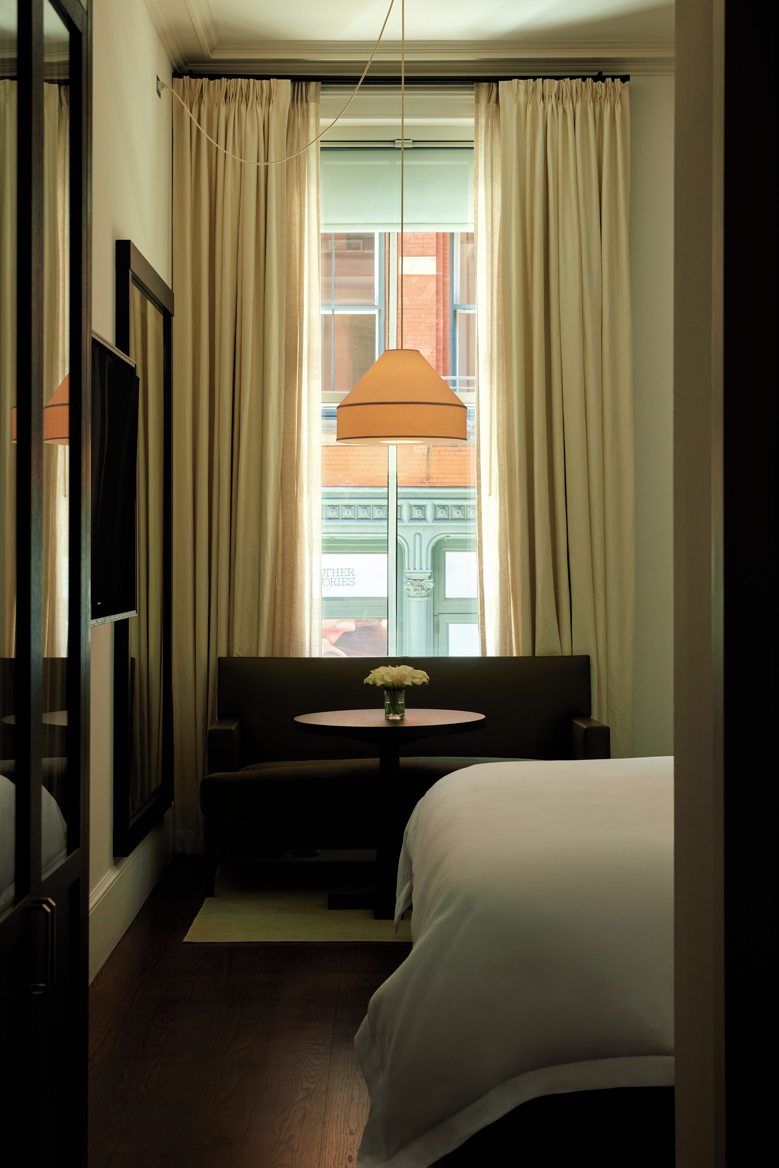 Ein Hotelzimmer mit Bett, einer Couch, einem kleinen Tisch mit Blumenvase und einem Fenster mit Vorhängen.