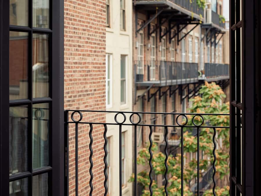 A view from a window with a black metal balcony railing, looking out at a brick building with multiple stories and balconies.