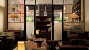 A modern lounge area with seating, a bookshelf, and large windows offering a view of the city. - The Mercer (New York)