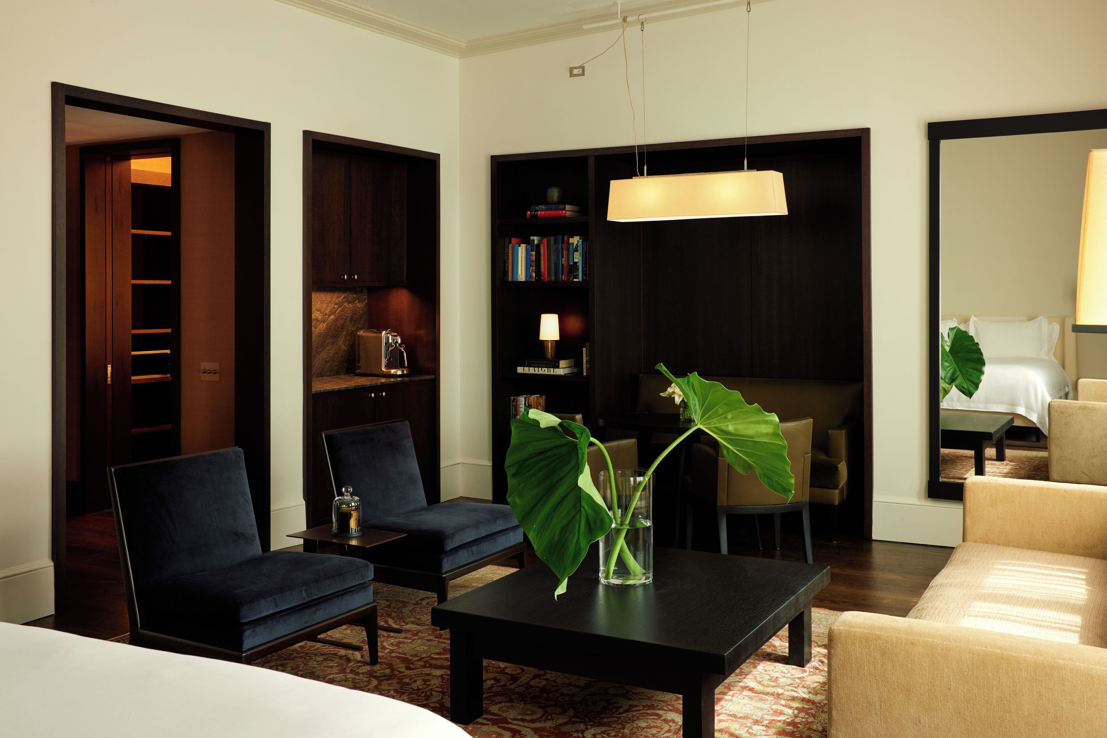Hotelkamer met een bed, twee fauteuils, een salontafel, een boekenkast, een bureau en een grote spiegel.