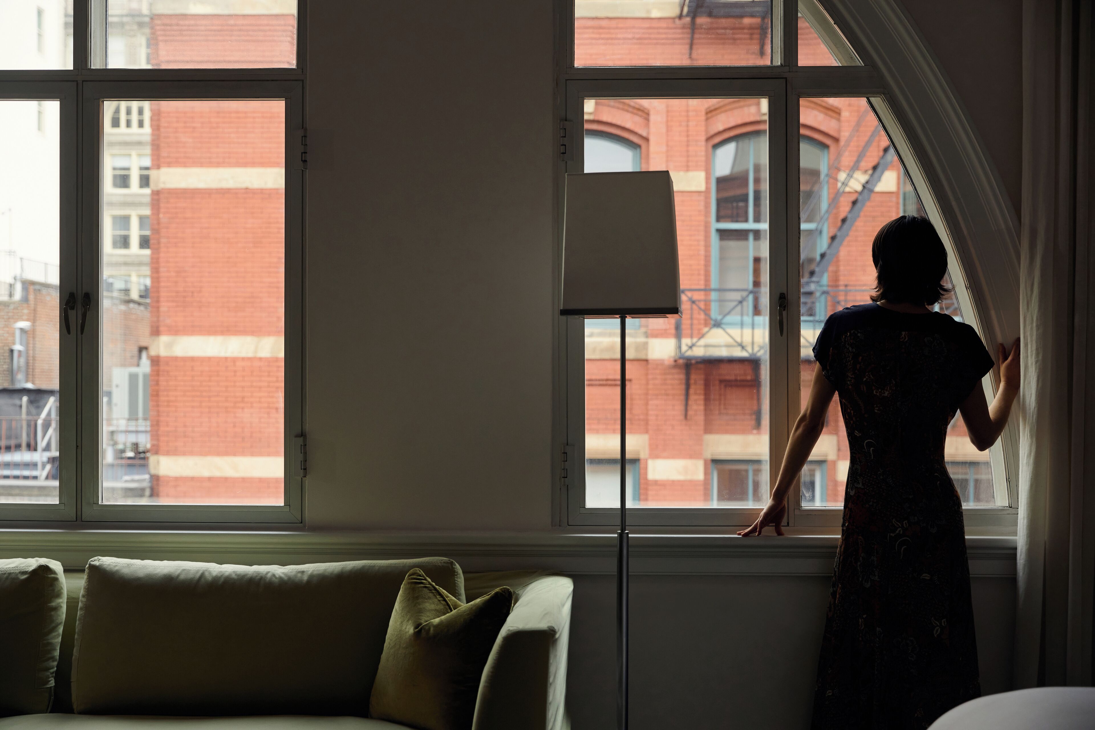 A room with a large window, a standing lamp, and a sofa.