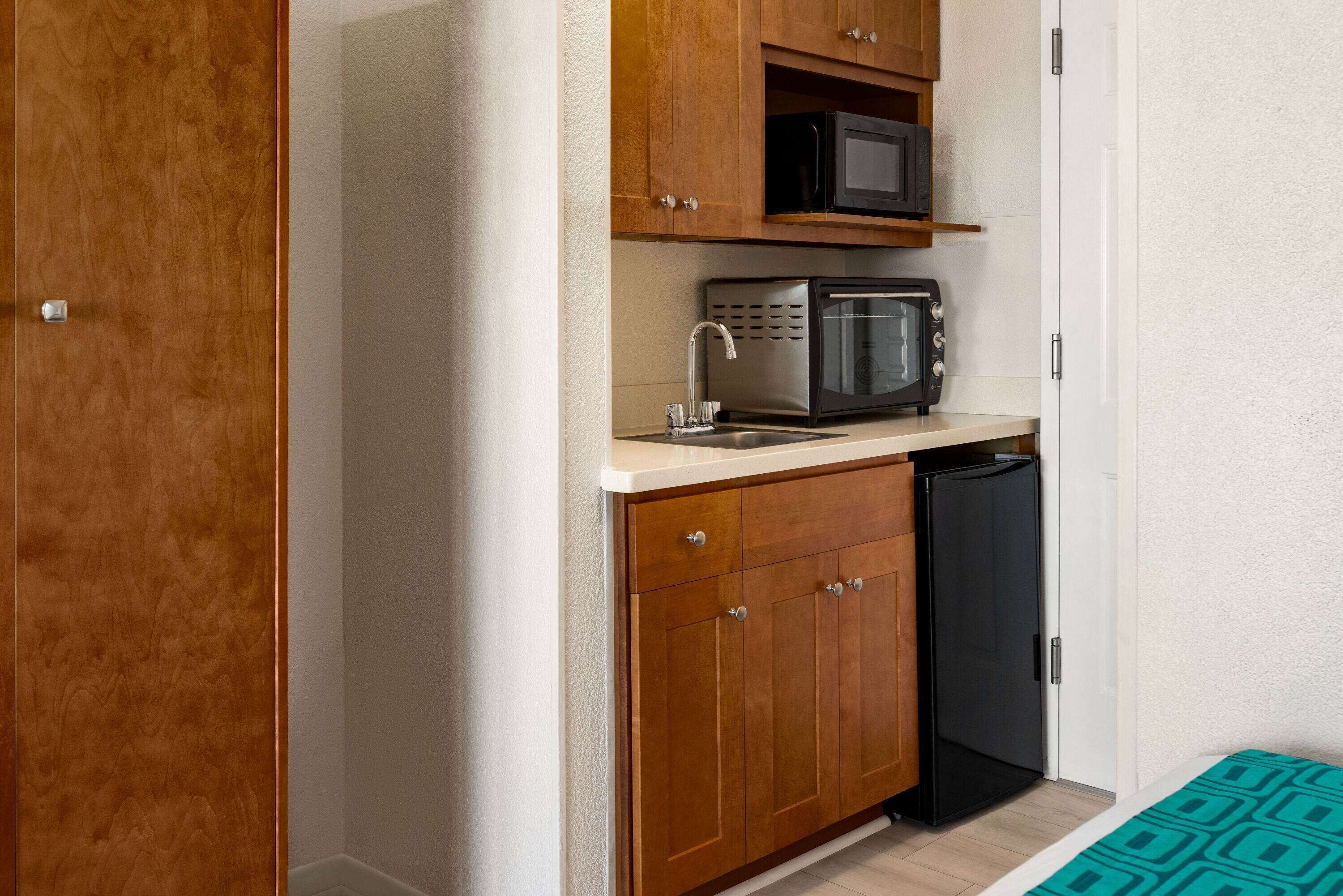 A compact kitchen with wooden cabinets, a microwave, and a black refrigerator.
