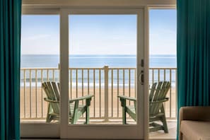 Une pièce donnant sur la plage grâce à une porte vitrée, deux fauteuils Adirondack verts et un canapé beige.