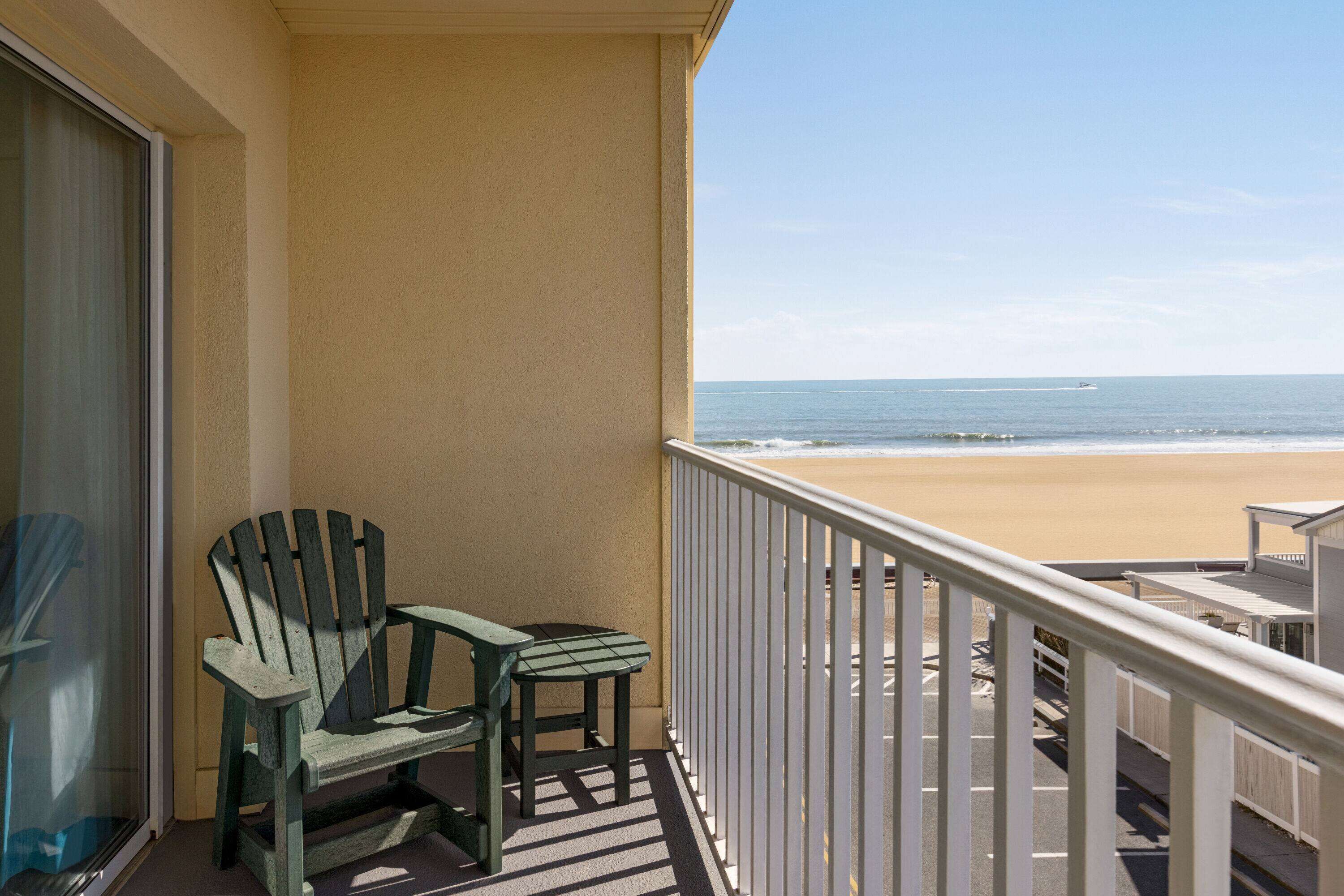 A balcony with a view of the beach, a chair, and a table.