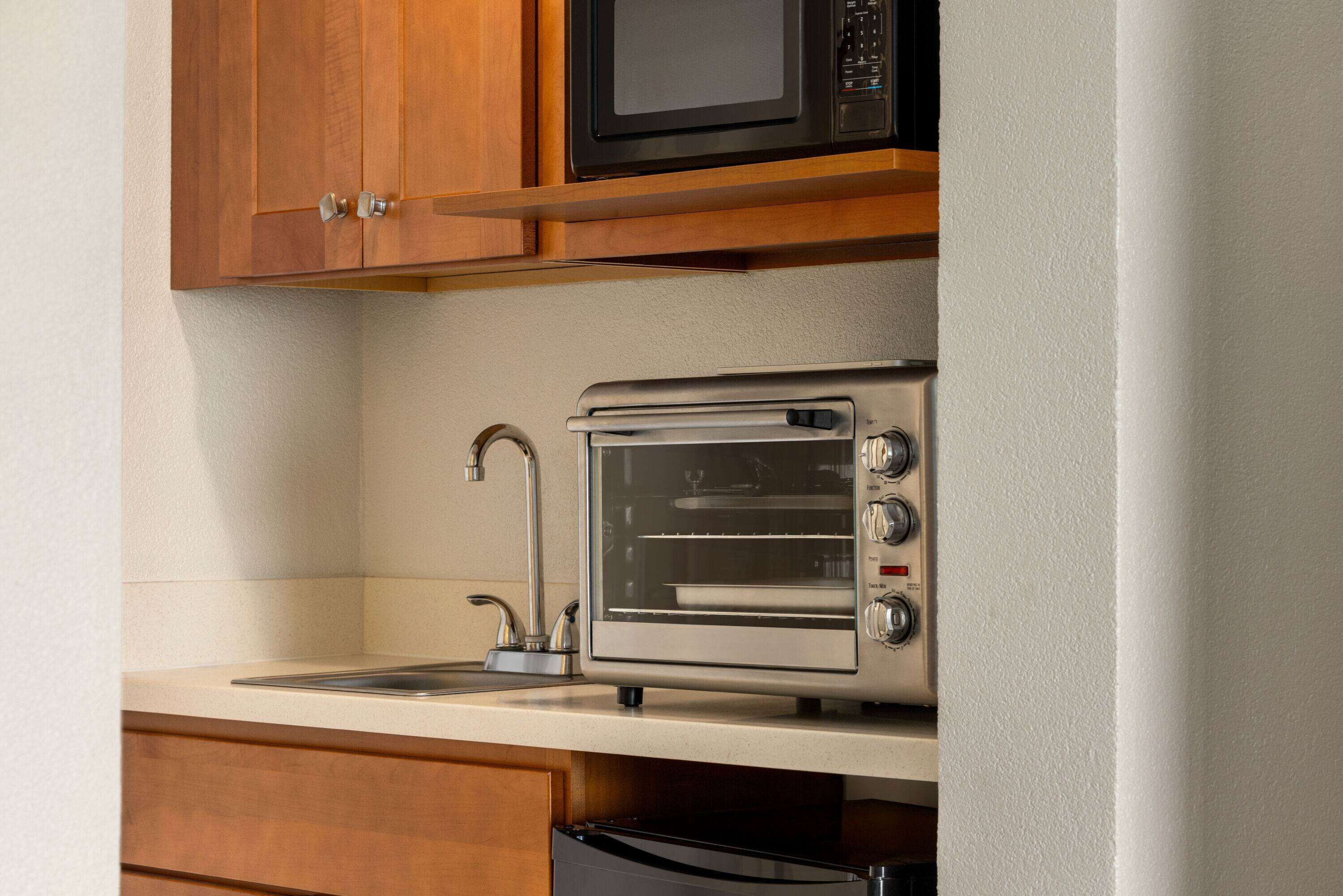 A kitchen with wooden cabinets, a stainless steel toaster oven, and a sink.