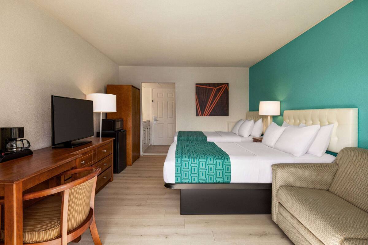 A hotel room with a bed, a desk with a television, a chair, a sofa, and a door leading to a bathroom.