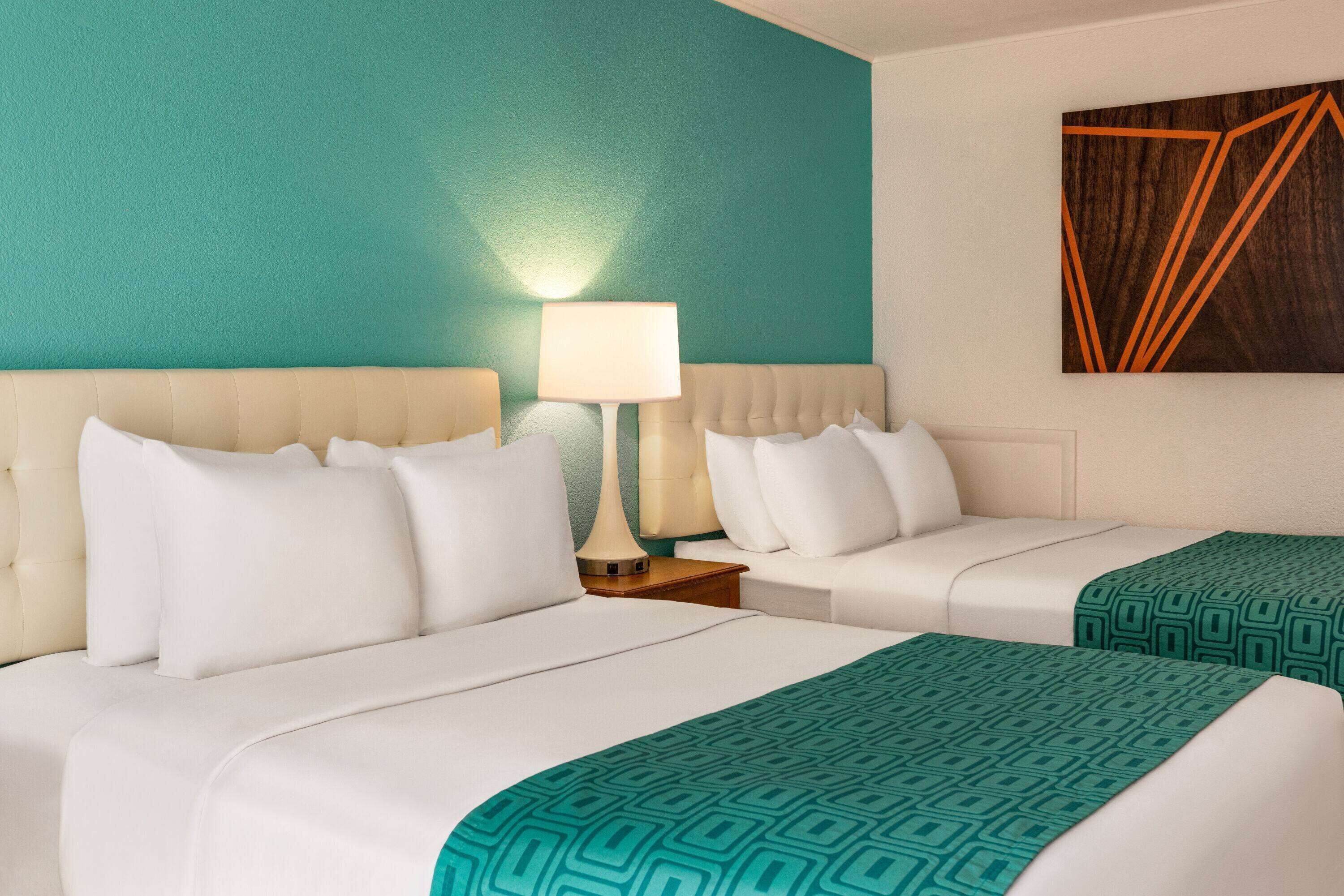 Une chambre d’hôtel avec deux lits, un mur d’accent de couleur turquoise et une œuvre d’art aux motifs géométriques.