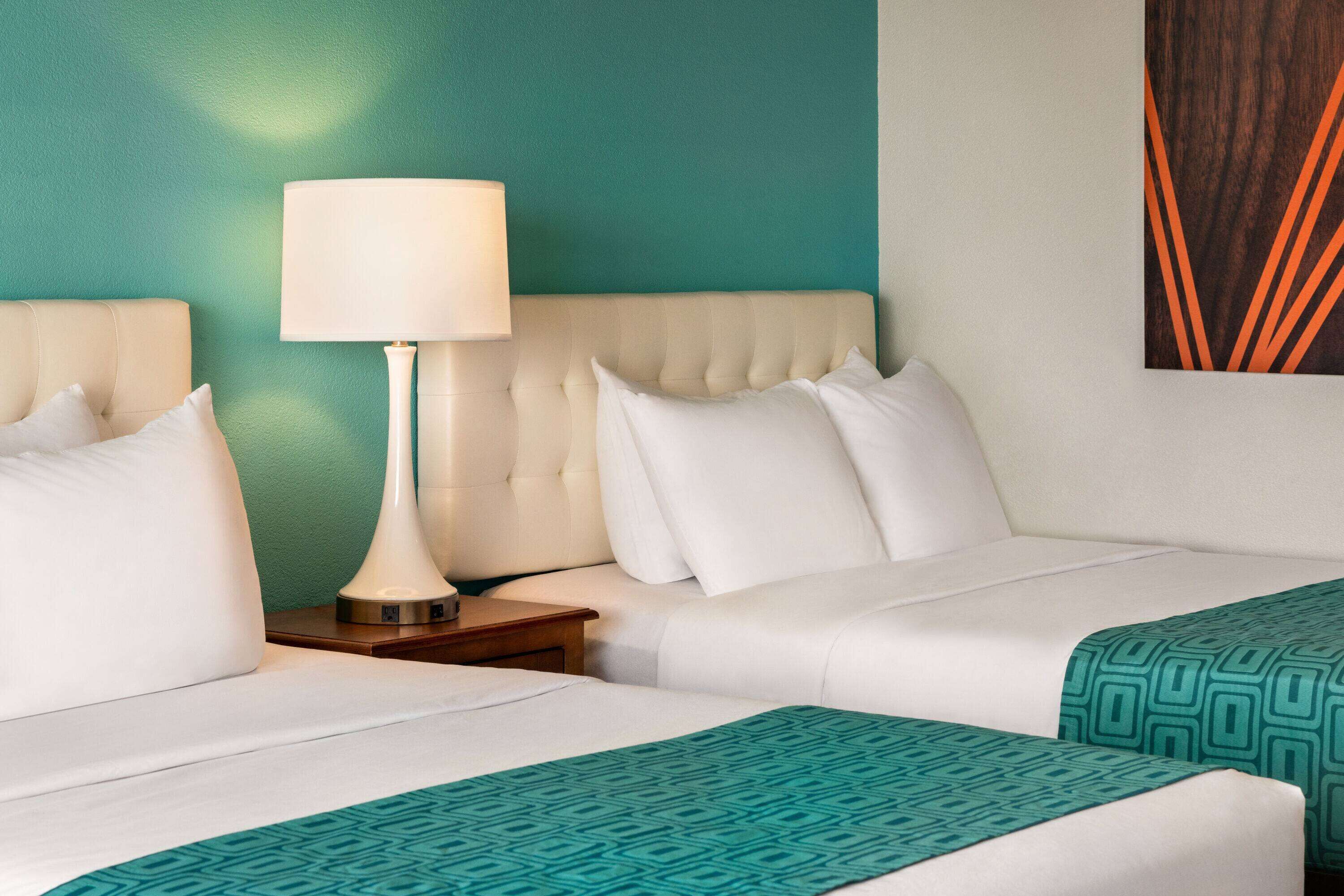 A hotel room with two beds, a nightstand, a lamp, and a wall with a geometric pattern.