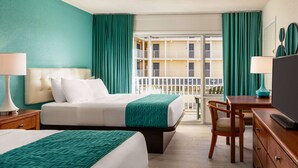 Habitación de hotel con dos camas, un escritorio, una silla, un televisor y un balcón con vista al edificio.