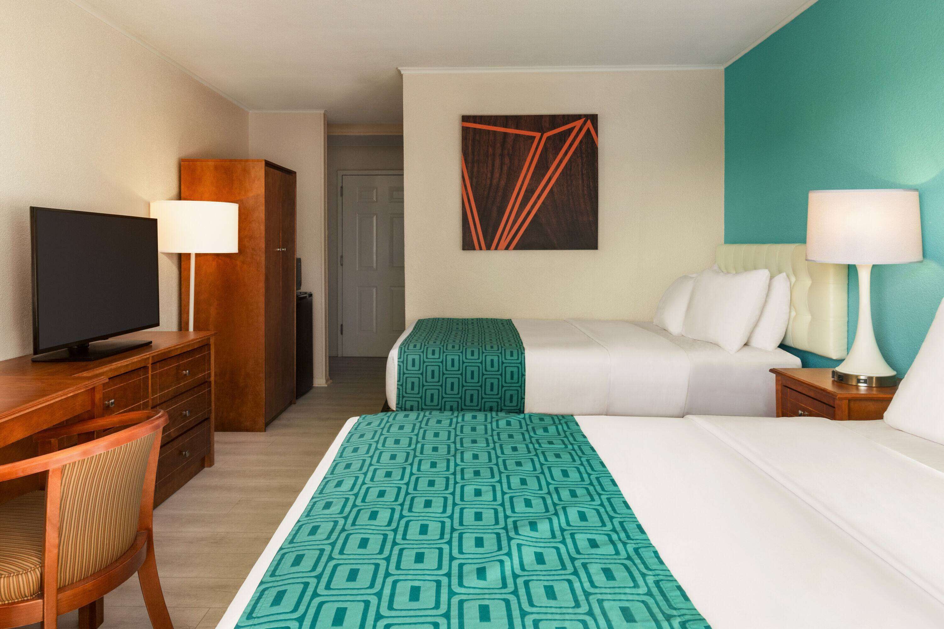A hotel room with a bed, a desk with a television, a chair, and two bedside lamps.