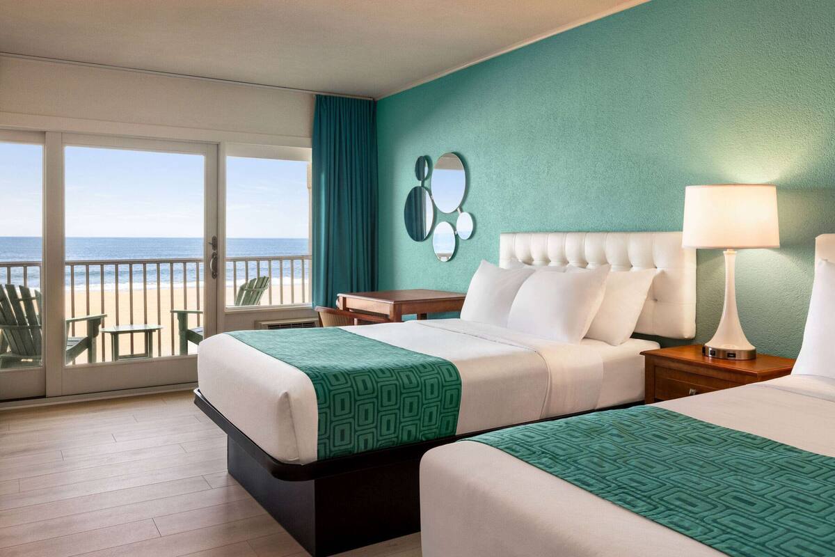 A hotel room with two beds, a view of the beach, a balcony, and a green wall.