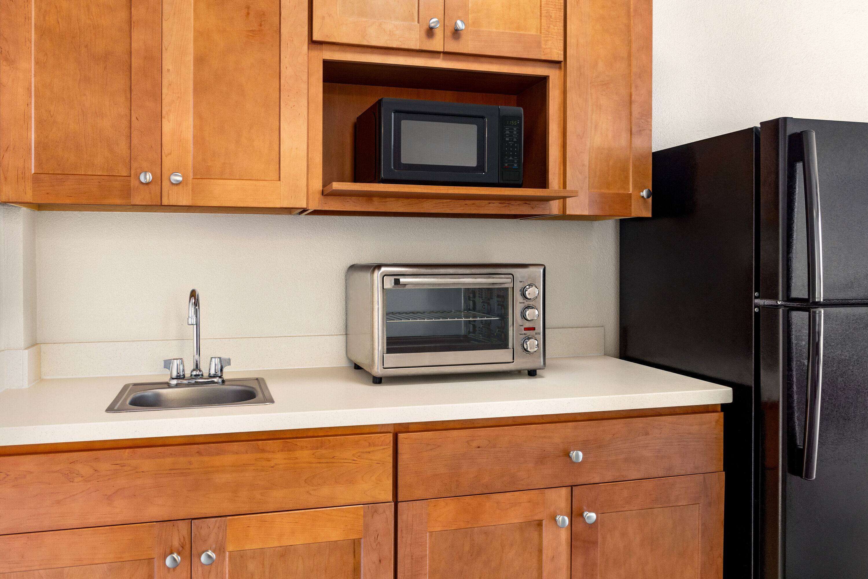 A kitchen with wooden cabinets, a black refrigerator, a microwave, and a toaster oven.