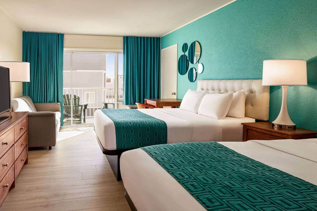 A hotel room with two beds, a TV, a dresser, a desk, and a balcony with a view.