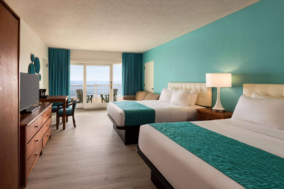 A hotel room with two beds, a desk, and a view of the ocean.