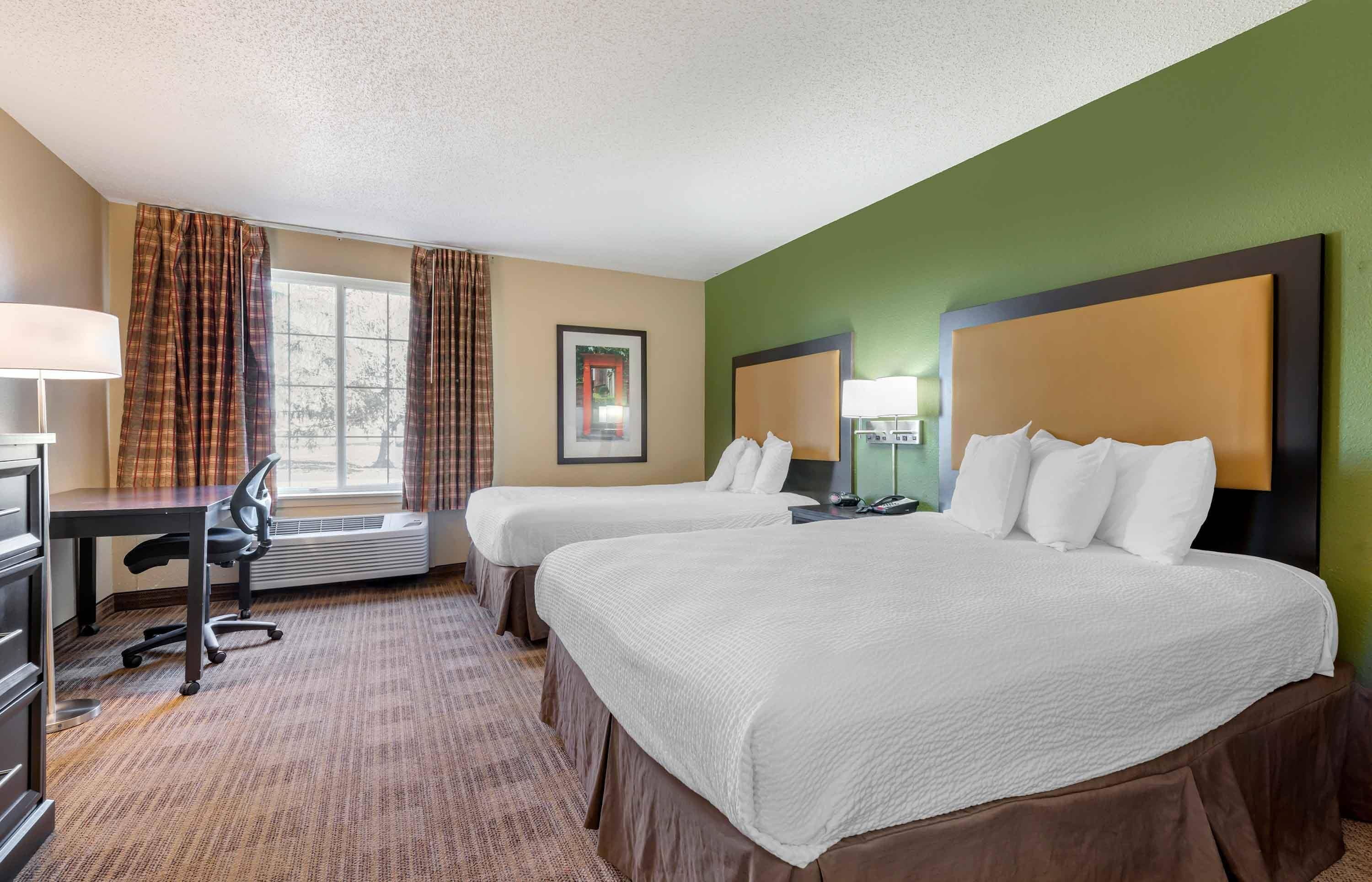 A hotel room with two beds, a desk, a chair, and a window with curtains.