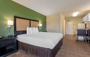 Una habitación de hotel con una cama grande, lámparas de noche, un escritorio pequeño y una kitchenette.