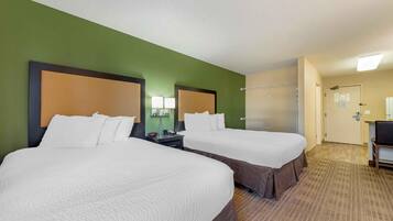 A hotel room with two beds, a desk, a chair, a lamp, and a door.