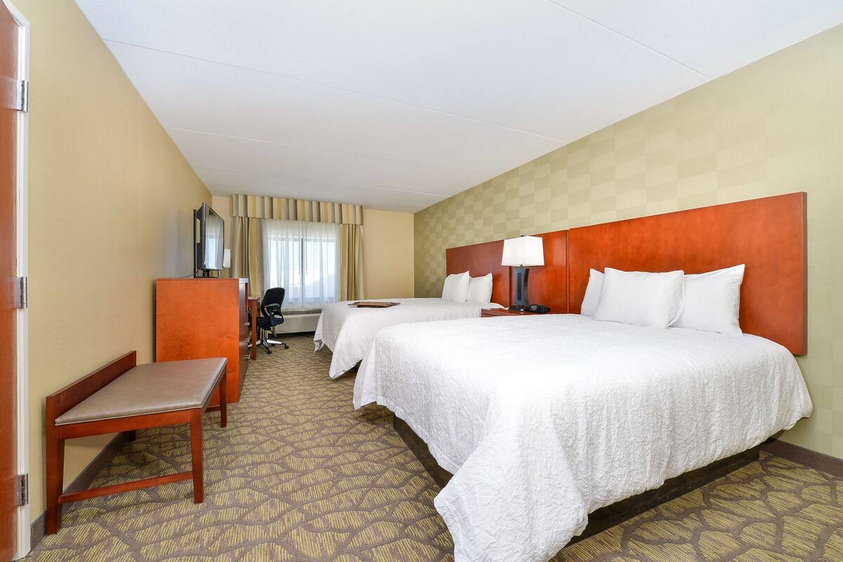A hotel room with two beds, a desk, a chair, a television, and a window with curtains.