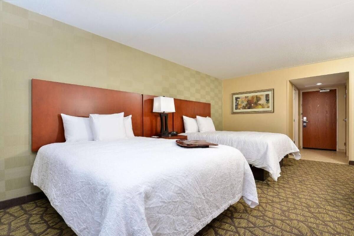A hotel room with two beds, a headboard, a lamp, a painting, and a door.