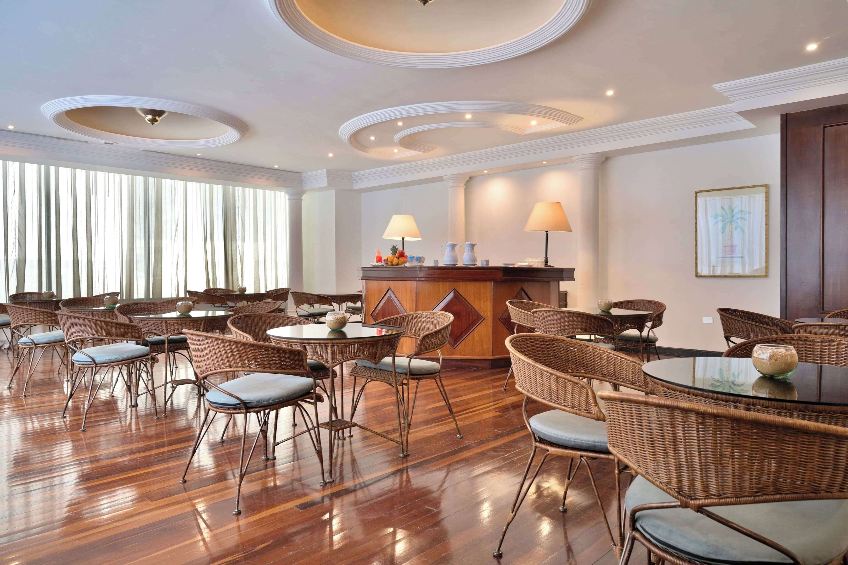 A hotel lobby with wicker chairs, a round table, and a reception desk with lamps.