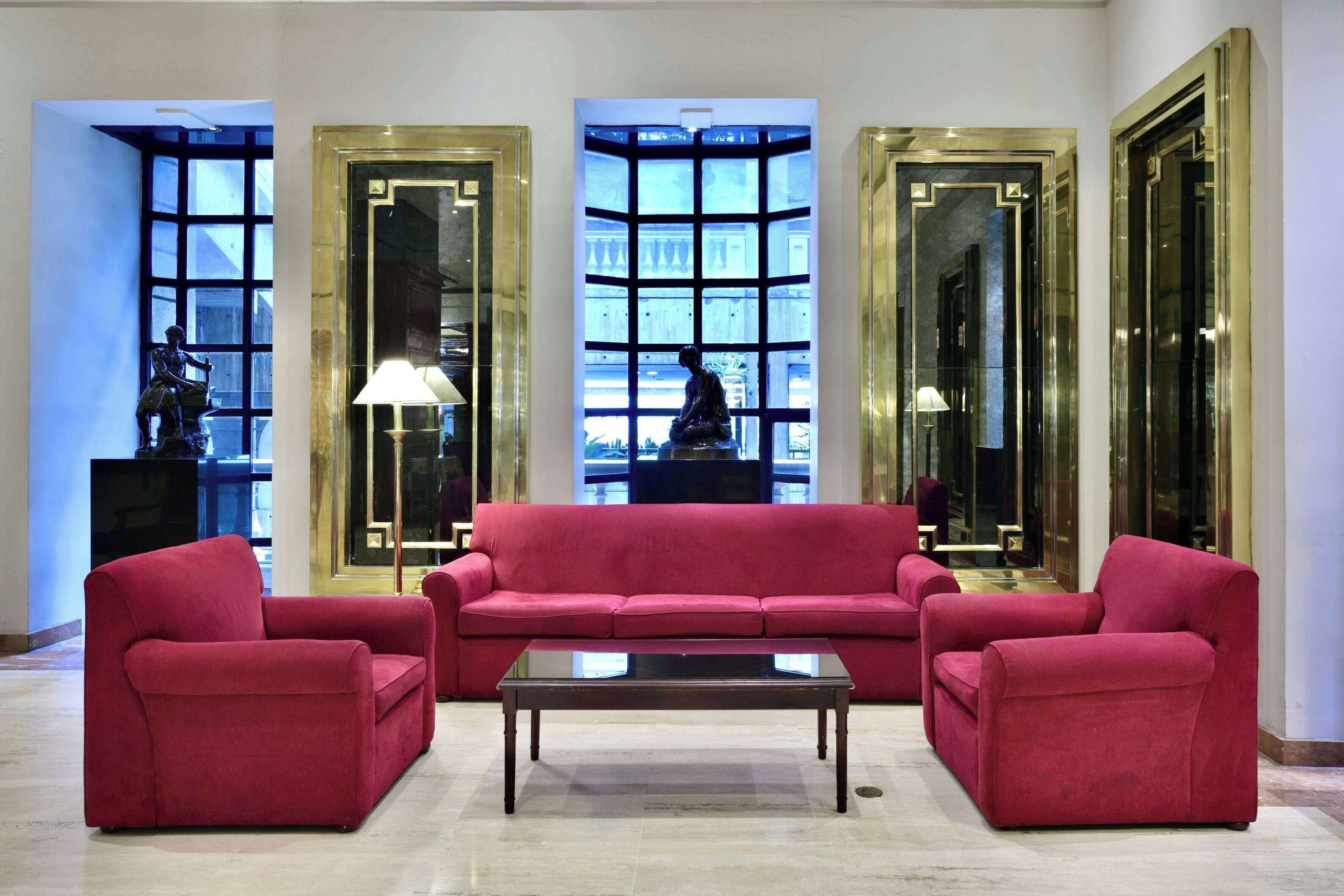 Un hall con un sofá rojo, una mesa de centro de vidrio y ventanas grandes con marcos decorativos.