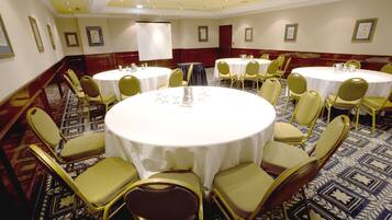 A conference room with round tables and chairs, a projector screen, and framed pictures on the walls.