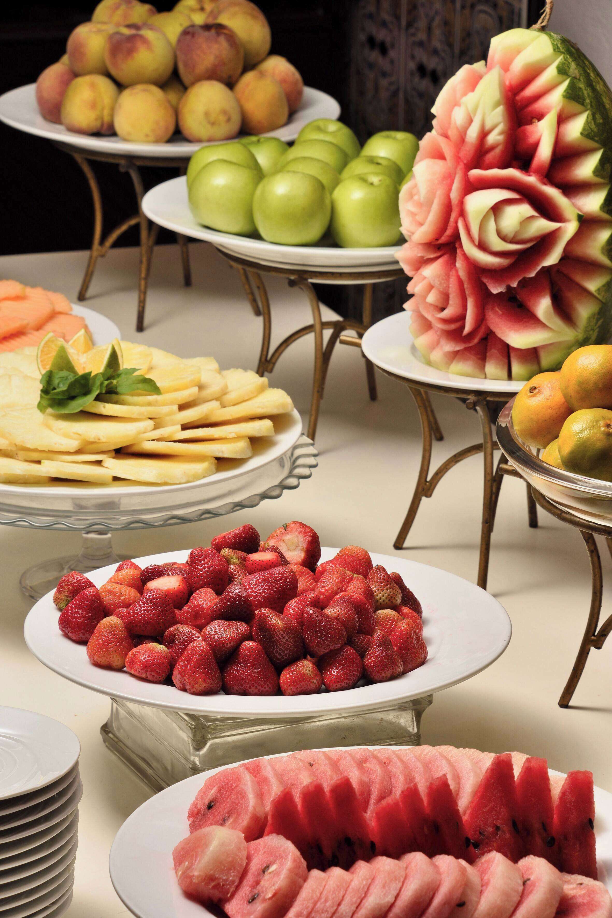 A table with various fruit displays including apples, strawberries, and a watermelon carved into a flower.