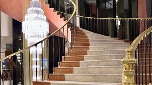 Eine prächtige Treppe mit Marmorstufen und einer goldenen Handlauf, die zu einem hochräumigen Bereich mit einem großen Kronleuchter führt.