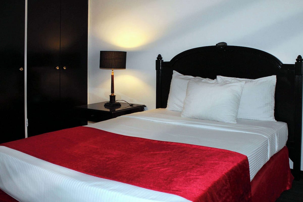 A hotel room with a large bed, a nightstand with a lamp, and dark wooden furniture.