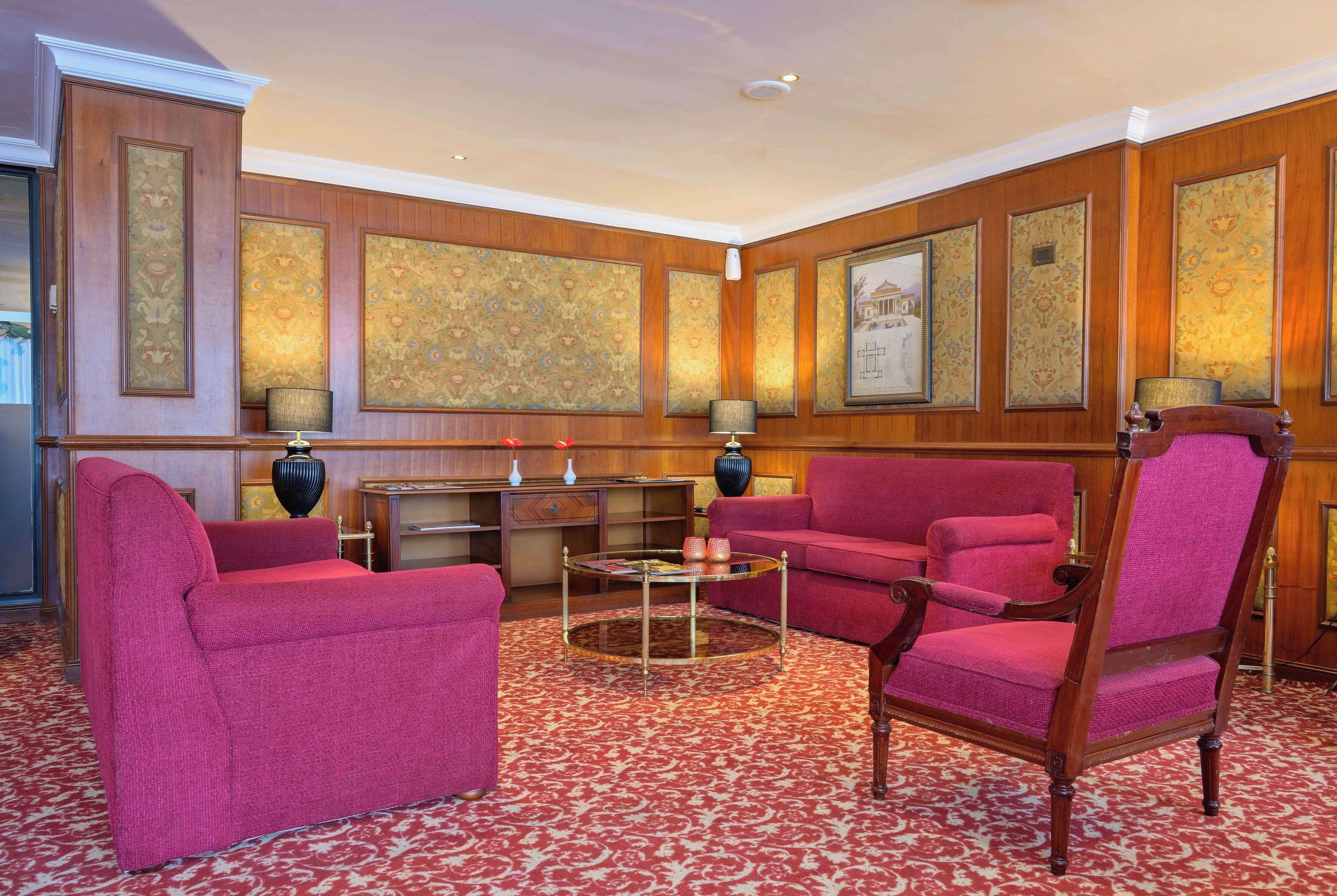 A room with a red carpet, two red sofas, a round coffee table, and wooden paneling on the walls.