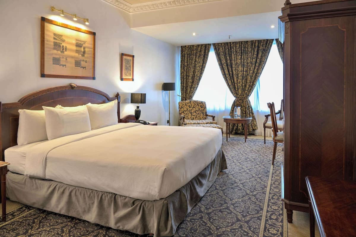 A hotel room with a large bed, a desk, a chair, and a wardrobe.