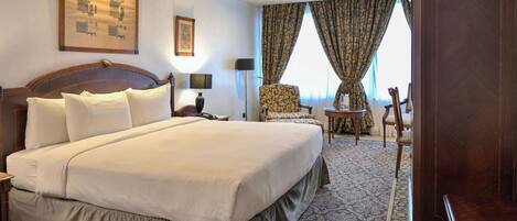 A hotel room with a large bed, a desk, a chair, and a wardrobe.