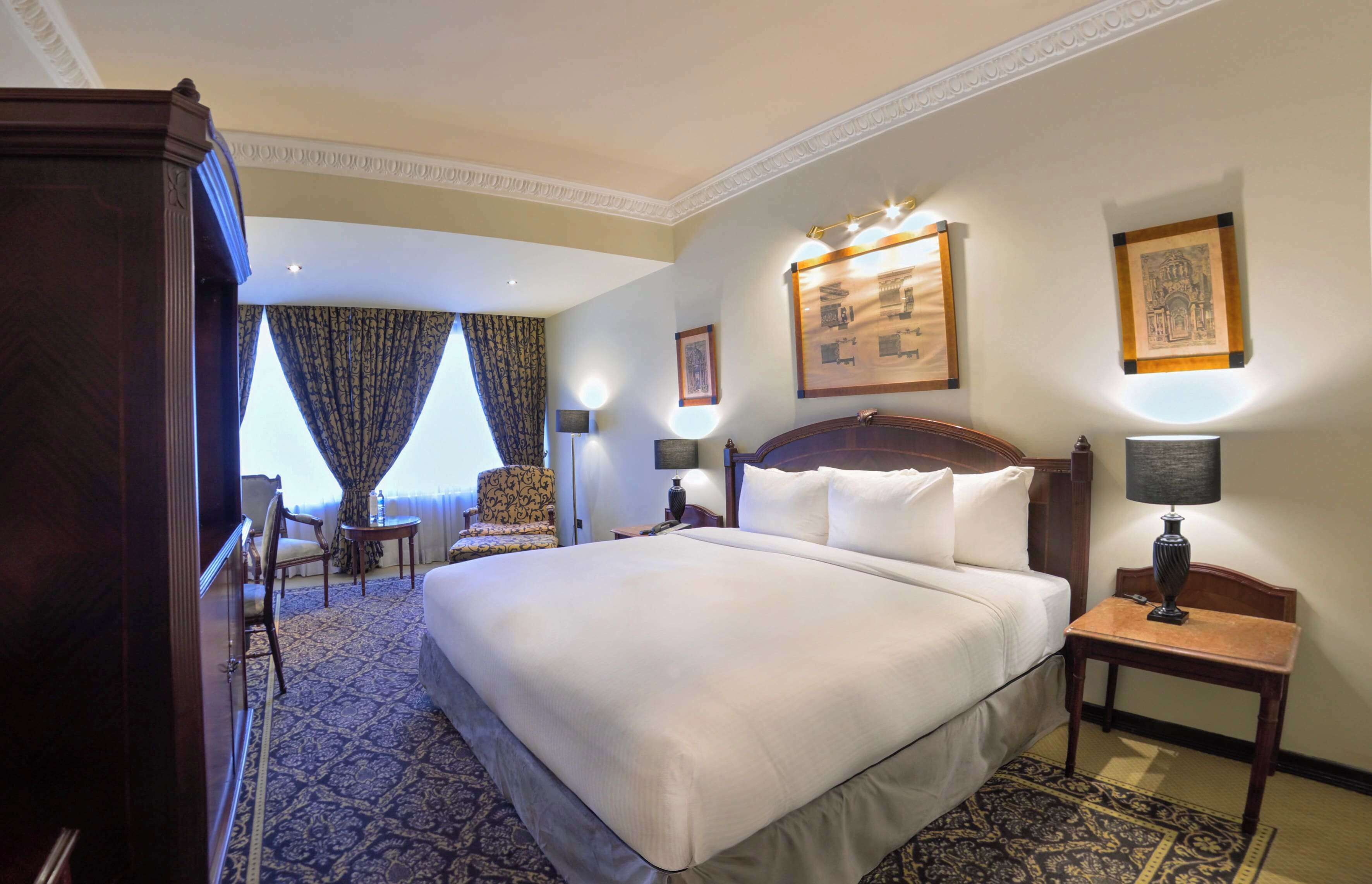 Ein Hotelzimmer mit einem großen Bett, einem Schreibtisch, einem Stuhl und einem Vorhangfenster.