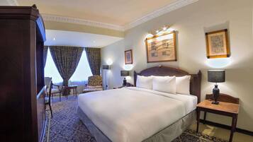 A hotel room with a large bed, a desk, a chair, and a window with curtains.
