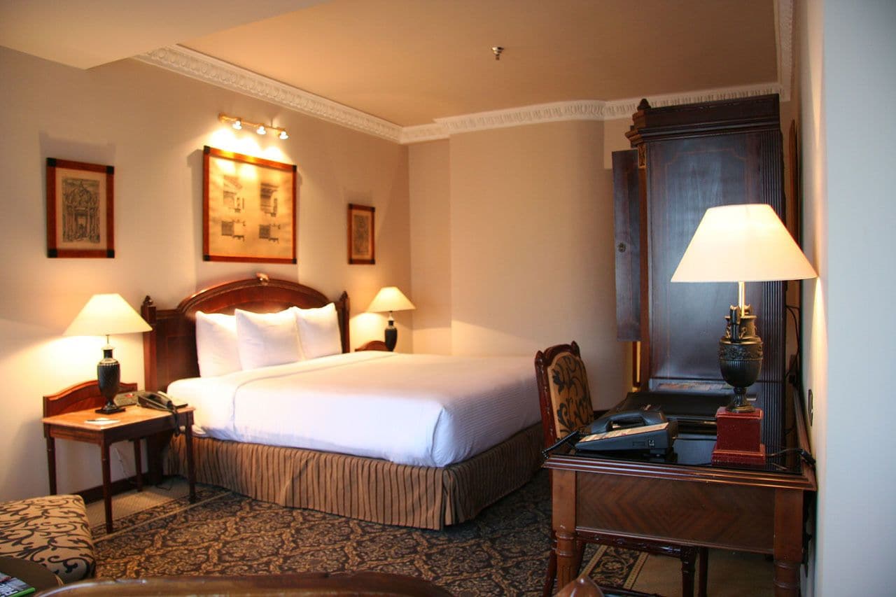 A hotel room with a large bed, two bedside tables with lamps, a wooden dresser, and a mirror.