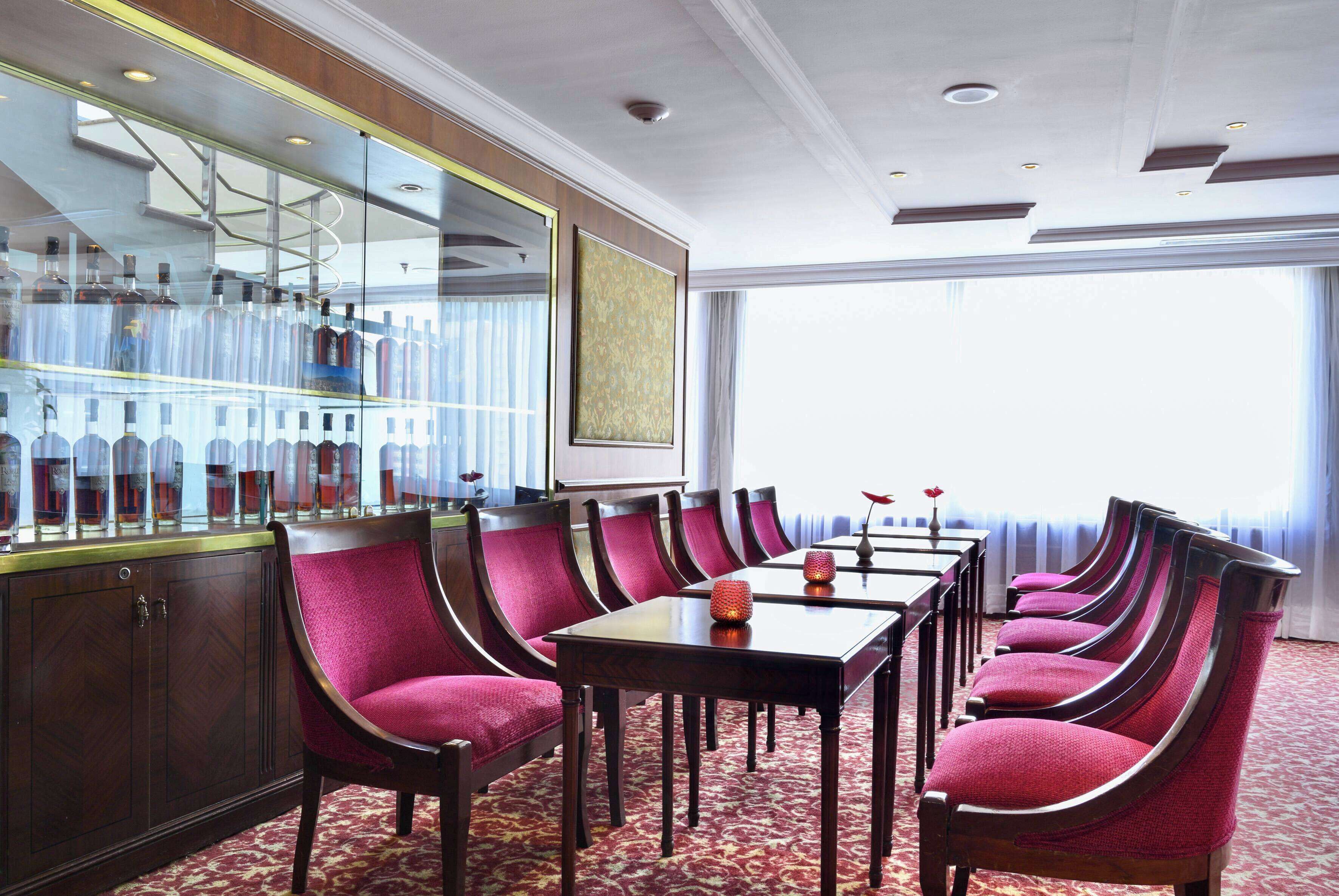 A conference room with a long table and matching chairs, a bar area with bottles, and a large window providing a view.