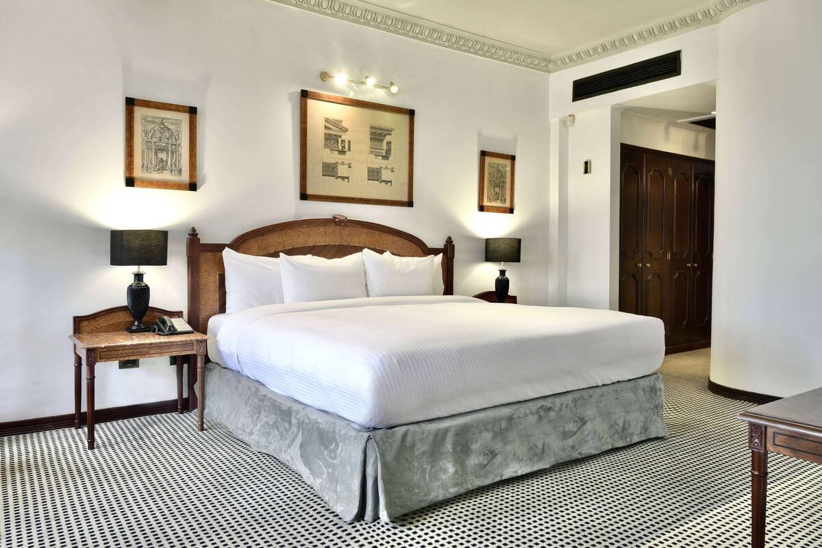 A neatly made bed with a wooden headboard, two bedside tables with lamps, and framed pictures on the wall.