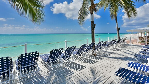 A deck with rows of white lounge chairs facing a turquoise sea under a clear sky. - Butterfly Beach Hotel (Oistins)