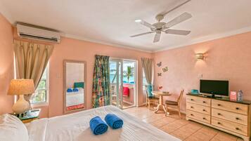 A hotel room with a bed, a ceiling fan, an air conditioner, a TV, a dresser, a chair, a table, and a balcony with a view.