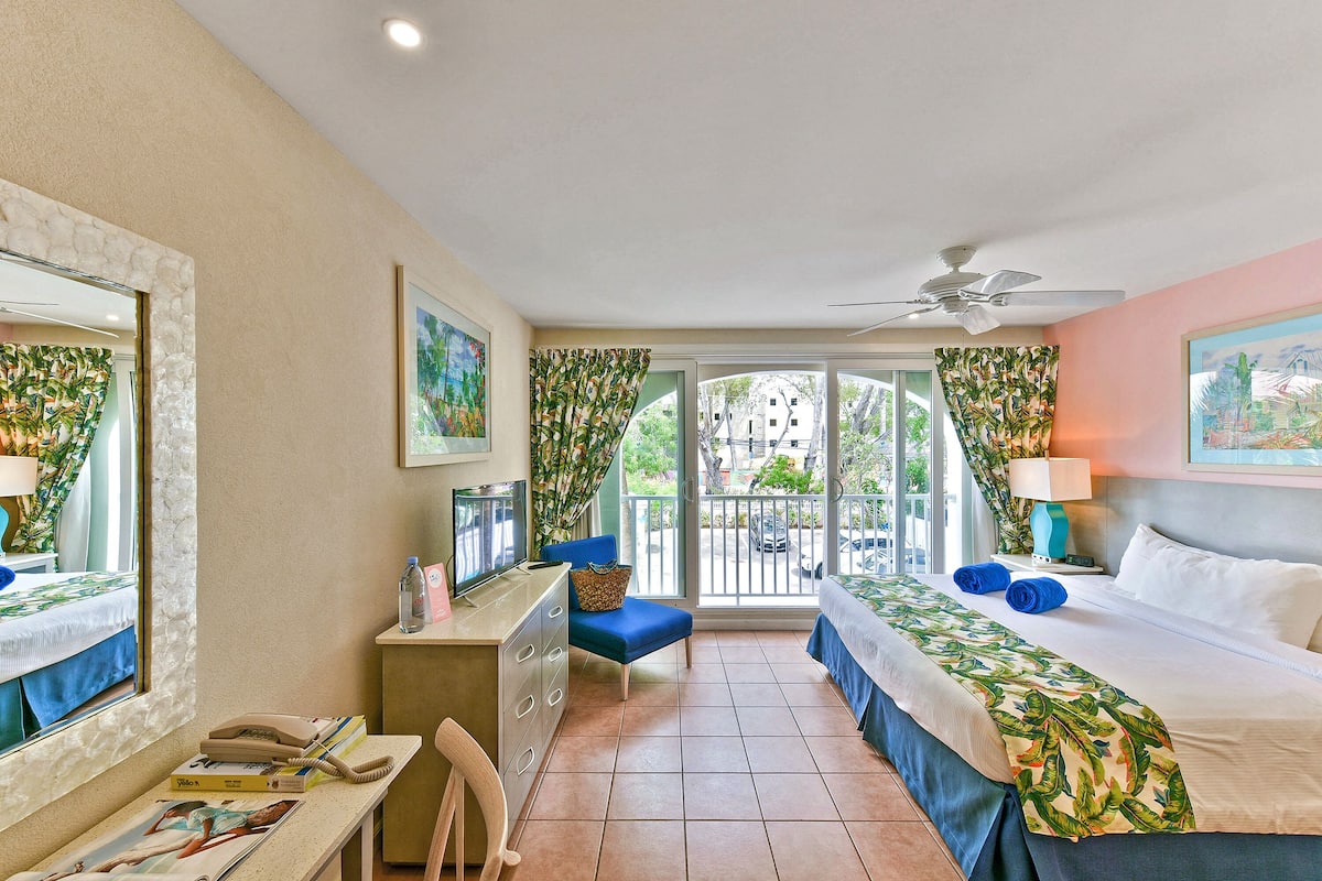 A hotel room with a bed, a desk, a chair, a window, and a balcony.