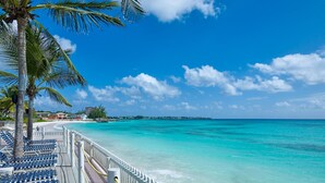 A beachside walkway with blue chairs and a white railing, leading to a turquoise sea. - Butterfly Beach Hotel (Oistins)