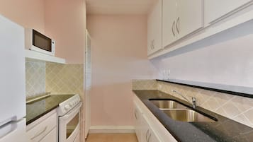 Une cuisine de taille réduite avec des meubles blancs, un four à micro-ondes, une cuisinière et un évier.