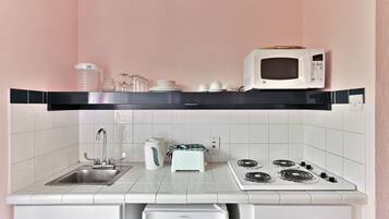 A compact kitchenette with a microwave, kettle, stove, sink, and a small refrigerator.