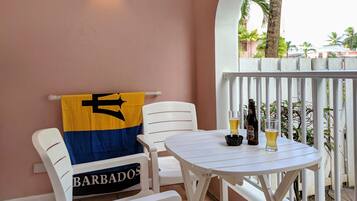 Un balcon avec une table blanche, deux chaises blanches, une serviette jaune et bleue, une bouteille de bière et un verre de bière.